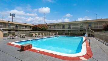 A swimming pool with a red and white edge, surrounded by a fence and a building with a sign that reads "B&B".
