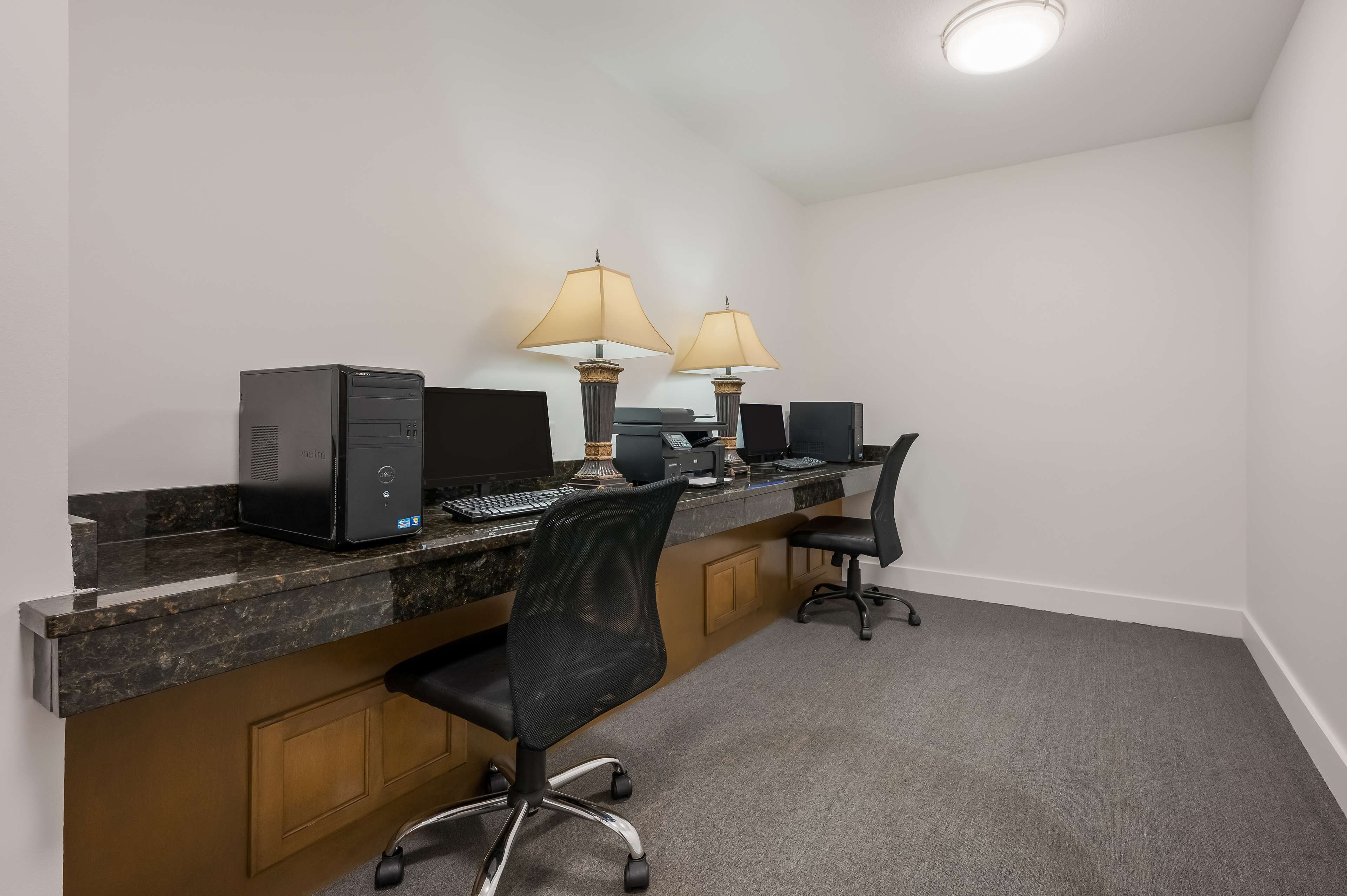 A workspace with two desks, computers, chairs, and lamps.