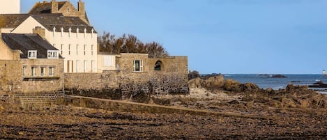 Un edificio costero con muros de piedra, una escalera de piedra y un litoral rocoso.