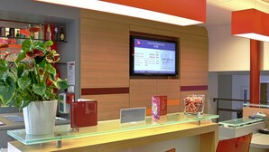 Una mesa de recepción de hotel con una pantalla digital, una planta en maceta y una vitrina de vidrio.