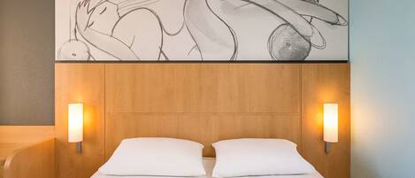 A hotel room with a wooden headboard, two bedside lamps, a large abstract painting above the bed, and a smartphone on the nightstand.