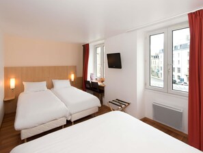 Habitación de hotel con dos camas, un escritorio con silla, televisión y ventana con cortinas.