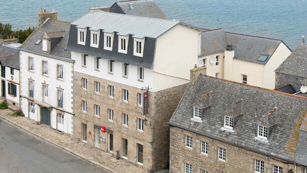 Un hotel frente al mar con varias edificaciones, incluyendo un edificio blanco destacado con techo gris y otro de color beige con techo gris.