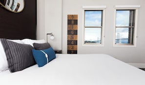 A bedroom with a bed, pillows, a wall-mounted light, a wooden number height chart, and two windows with a view of a bridge.