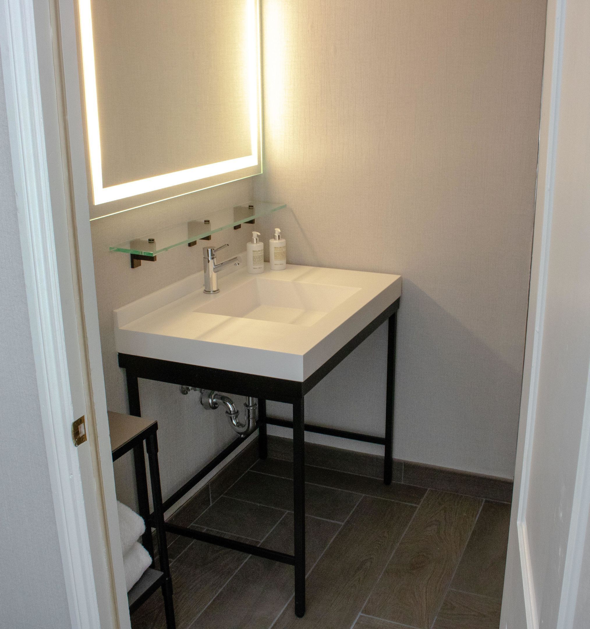 A bathroom with a white sink, a mirror, and a glass shelf above the sink.