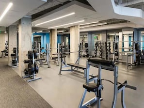 A spacious gym with various exercise equipment, large windows, and a high ceiling. - Harbor Court Hotel (San Francisco)