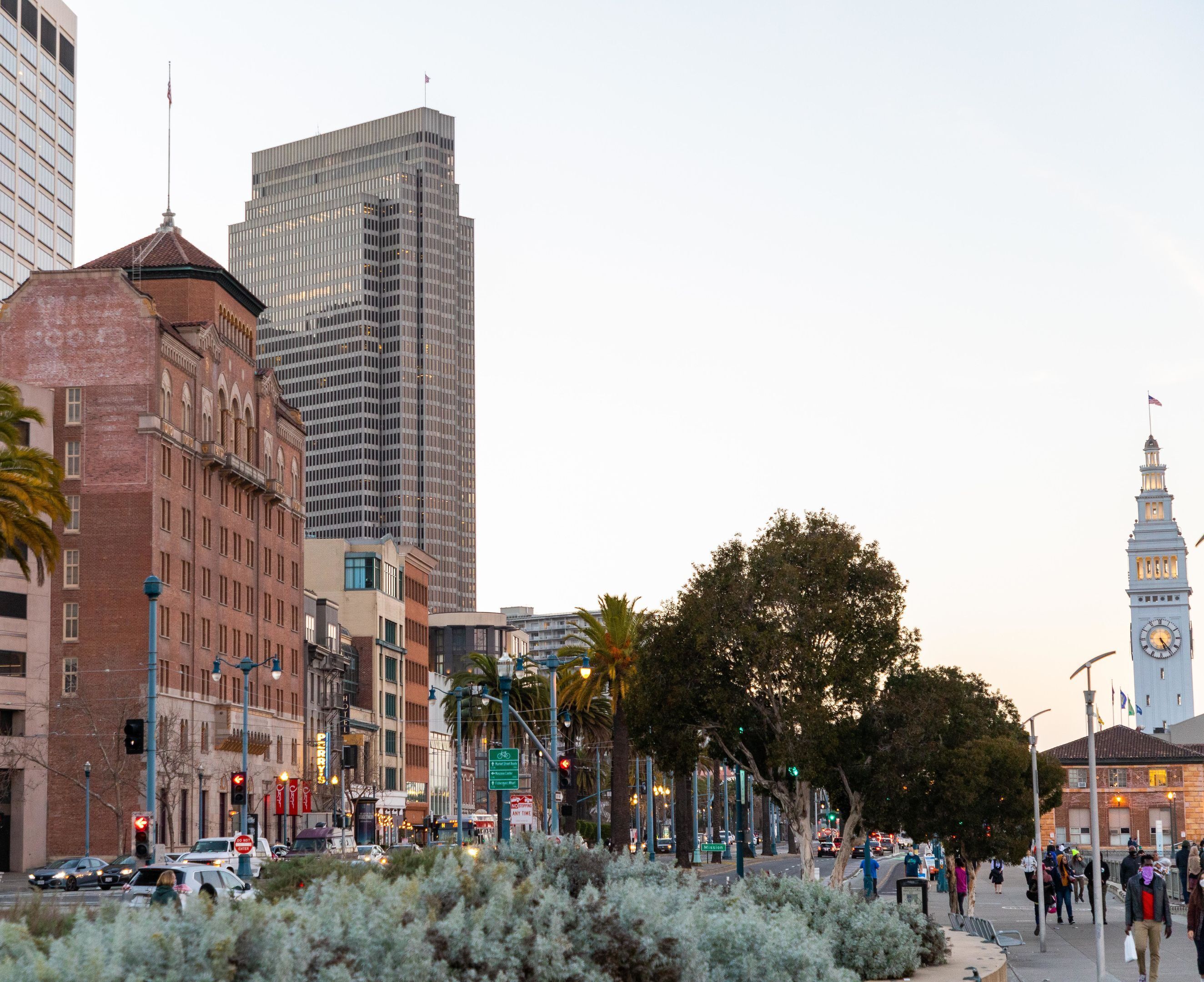 A city street with tall buildings, a clock tower, and pedestrians.