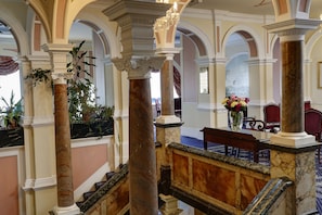 A grand lobby with marble columns, a staircase, and a seating area with a vase of flowers. - Royal Victoria Hotel (St Leonards-On-Sea)