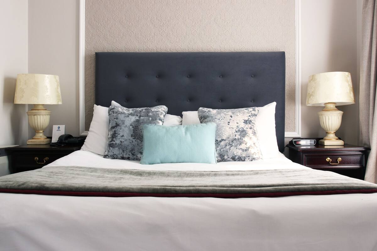 A neatly made bed with a dark headboard, multiple pillows, and two bedside tables with lamps.