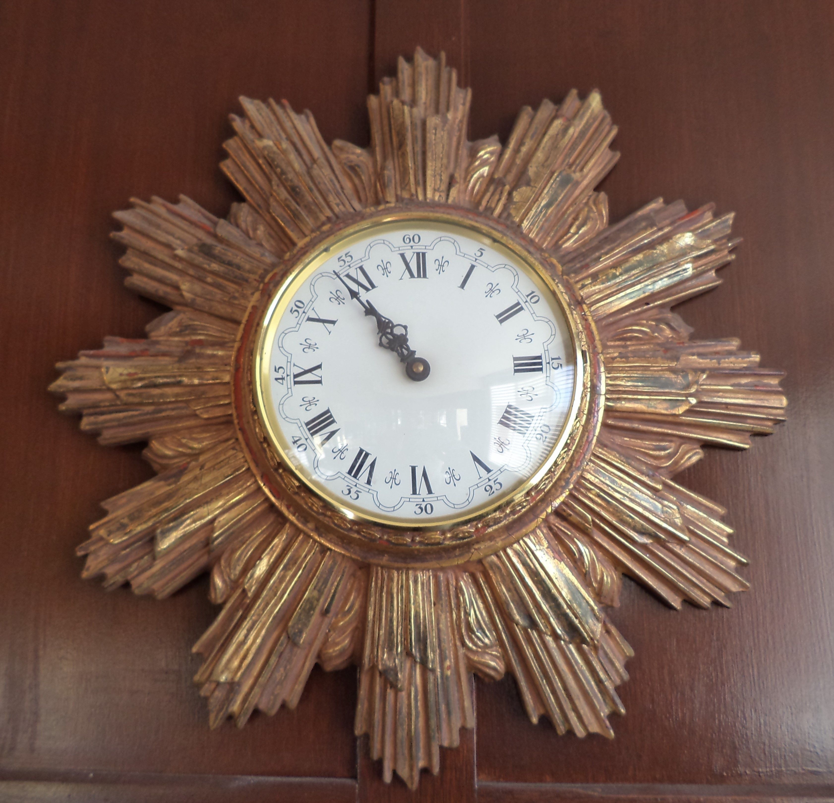 A wall clock with a sunburst design and Roman numerals.