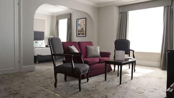 Habitación de hotel con un sofá rojo, dos sillones, una mesita y una cama al fondo.