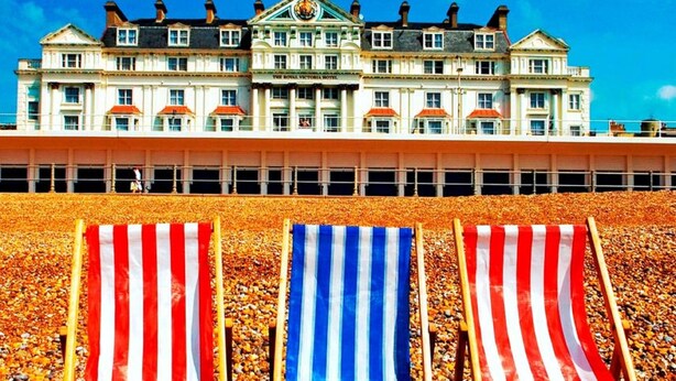 Tres sillas de playa con toallas a rayas frente a un gran edificio de hotel.