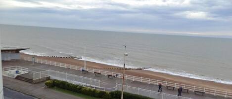 A coastal promenade with a sea view, benches, and a white fence along the walkway.
