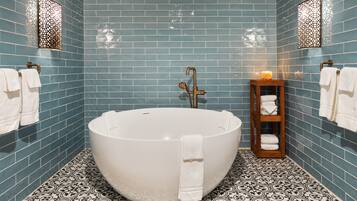 A bathroom with a freestanding bathtub, blue tiled walls, patterned floor tiles, and a wooden towel rack with towels.