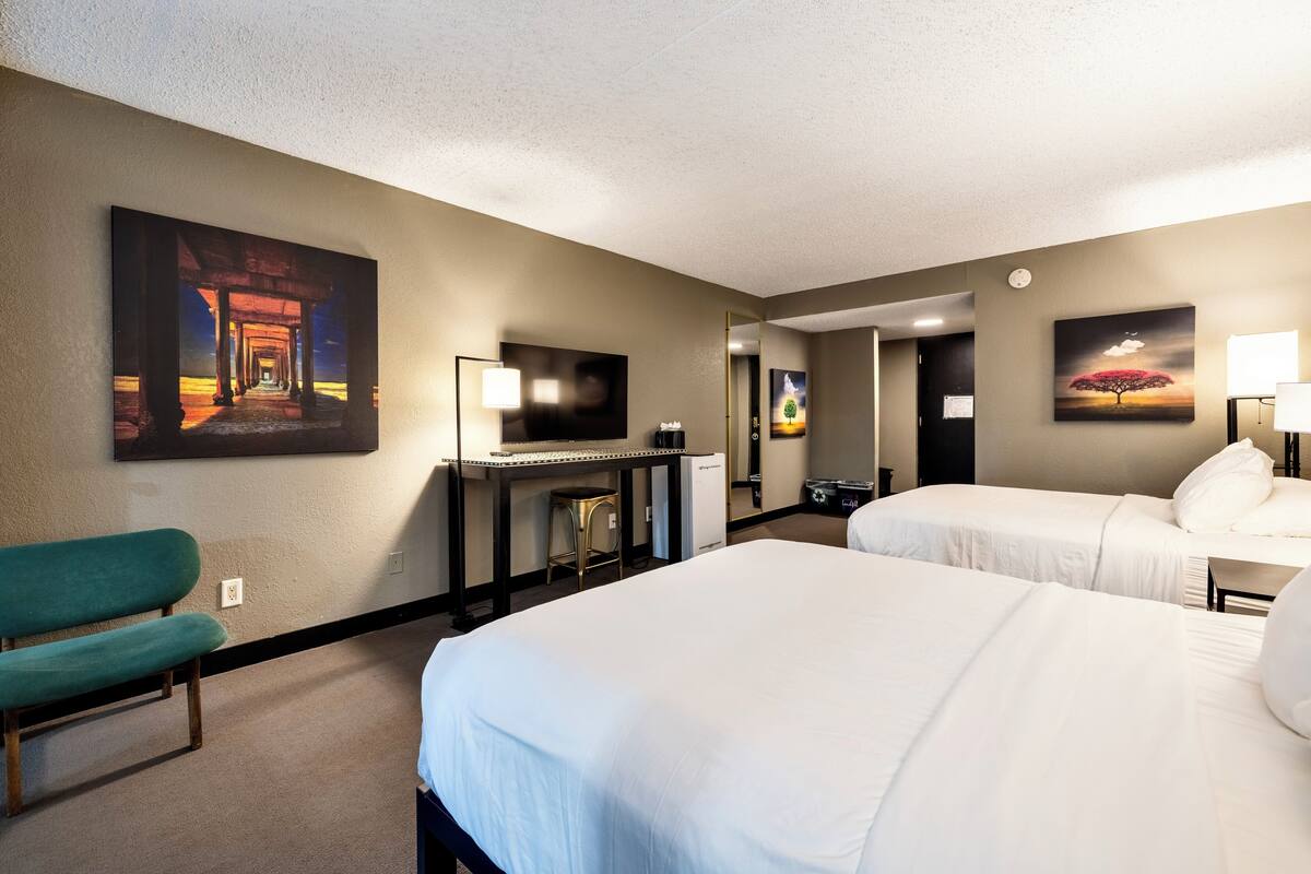 Une chambre d’hôtel avec deux lits, un bureau, une chaise et des œuvres d’art accrochées aux murs.