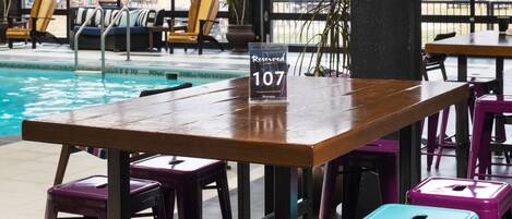 A poolside area with a wooden table and colorful stools, a 'Reserved 107' sign, and lounge chairs in the background.