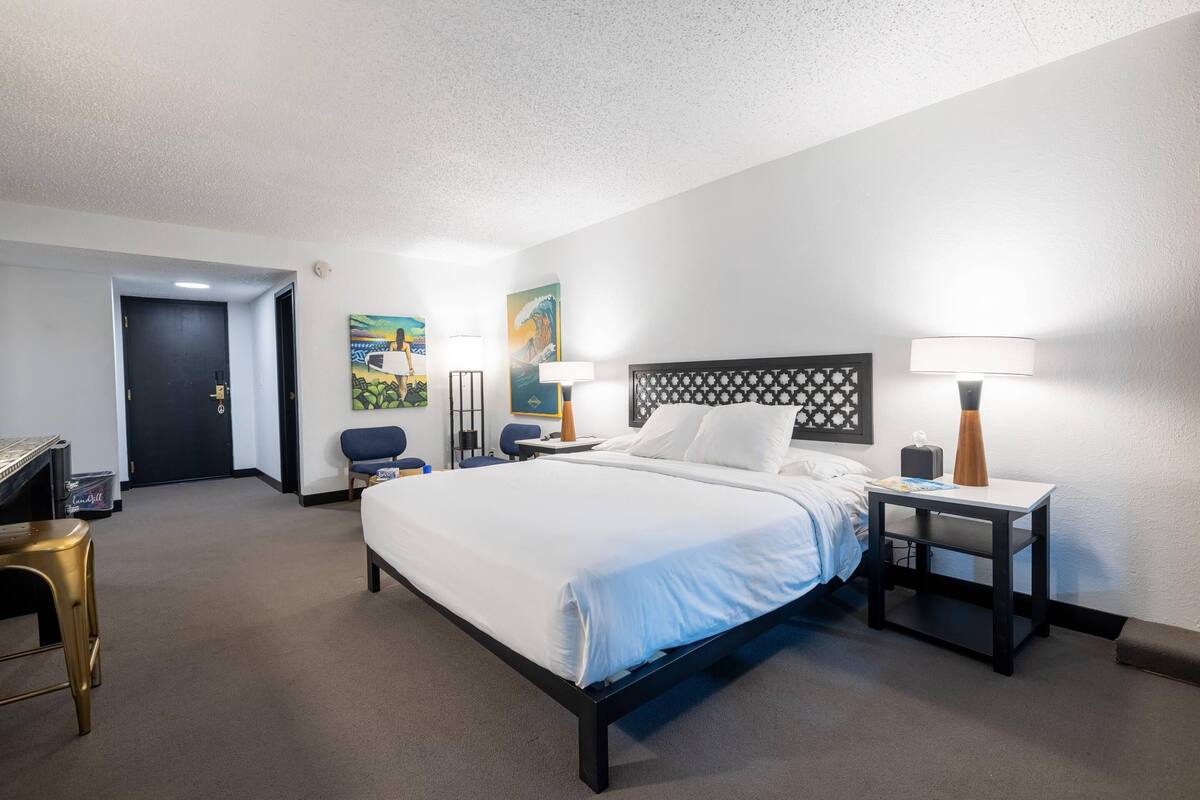Une chambre d’hôtel comprenant un lit, deux tables de chevet, un bureau, une chaise et des œuvres d’art accrochées aux murs.