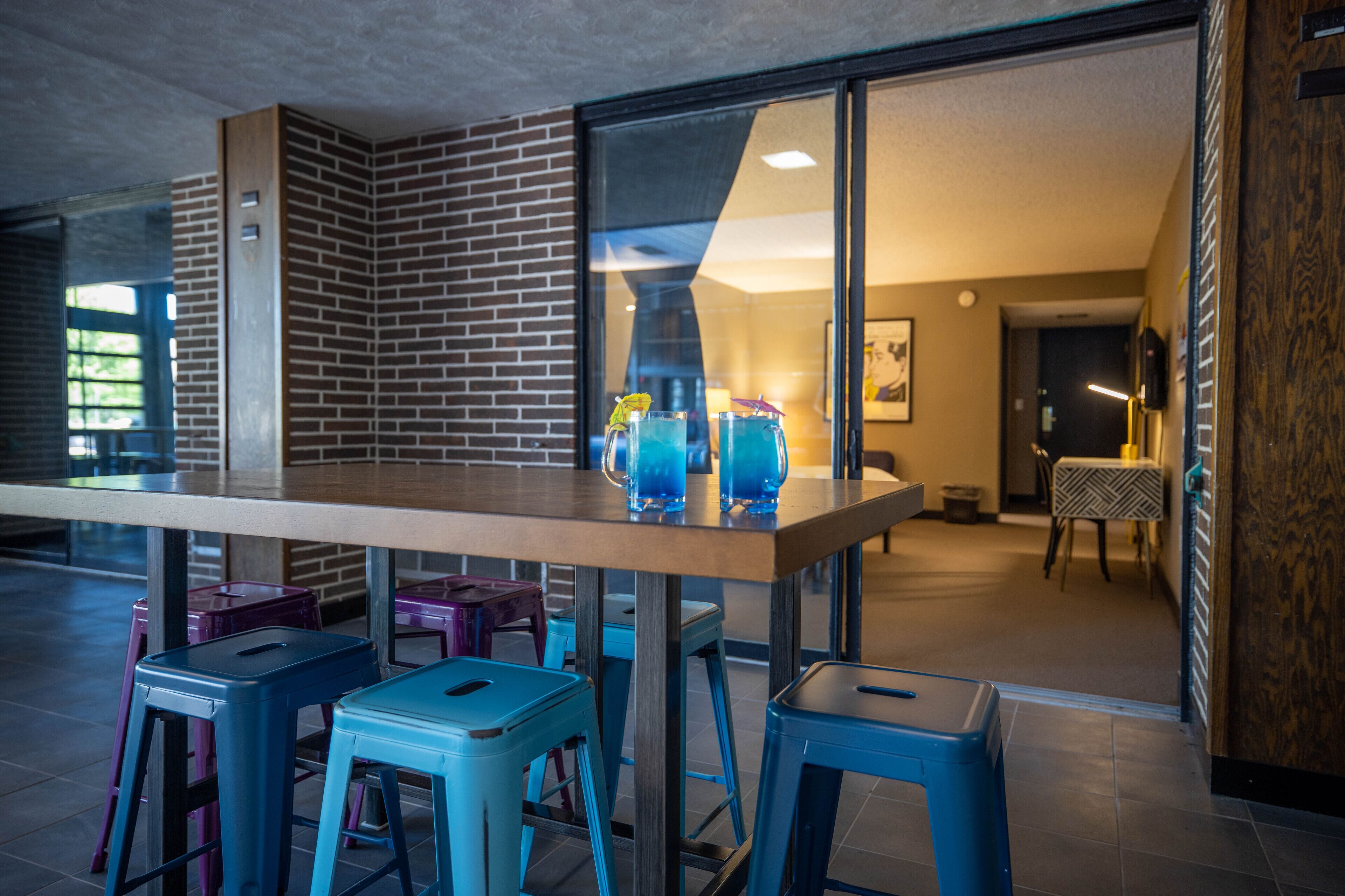 A modern bar area with a wooden table, blue stools, and a glass display case.