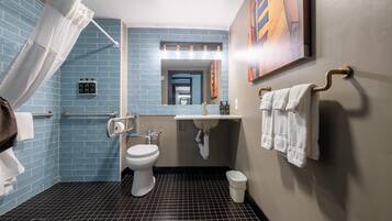 A modern bathroom with a blue-tiled wall, a white toilet, a sink with a mirror above it, and a shower area with a curtain.
