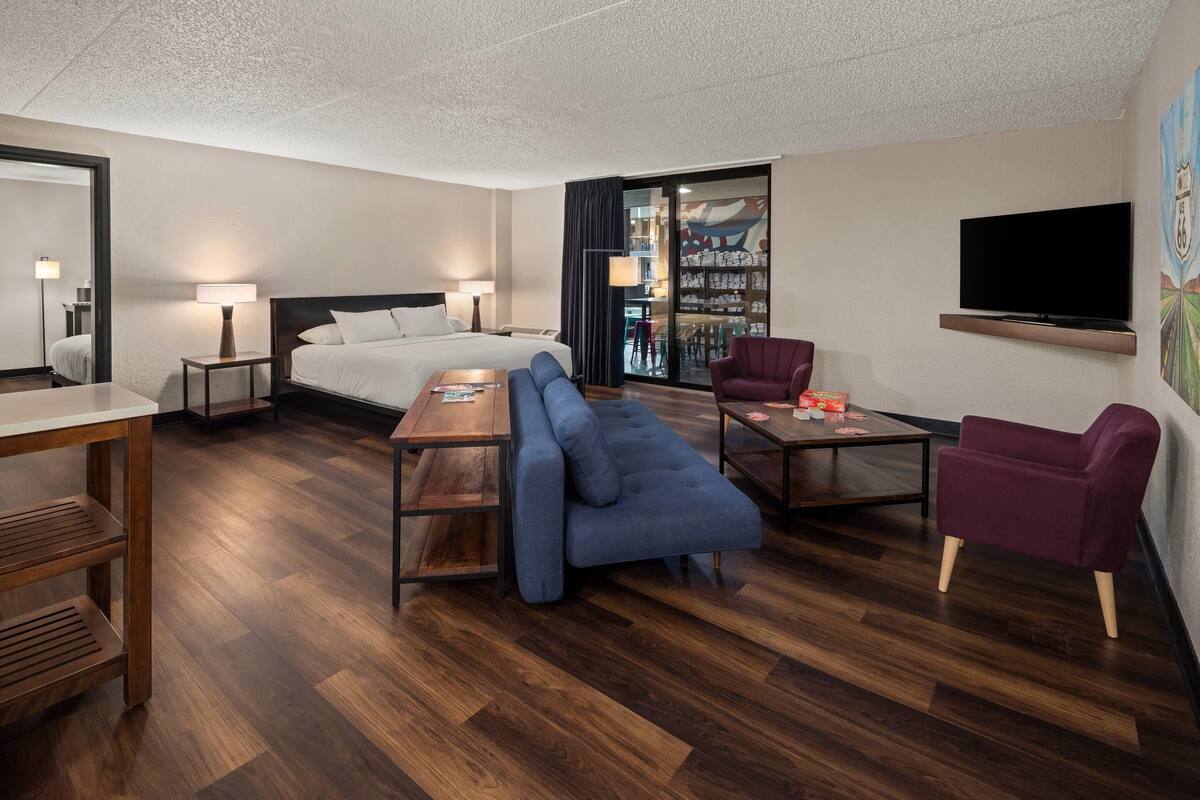 Une chambre d’hôtel moderne équipée d’un lit, d’un canapé, d’un fauteuil et d’un téléviseur fixé au mur.