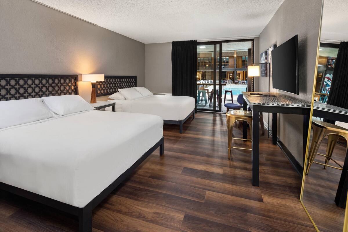 Une chambre d’hôtel avec deux lits, un bureau, une télévision et un balcon donnant sur une piscine.