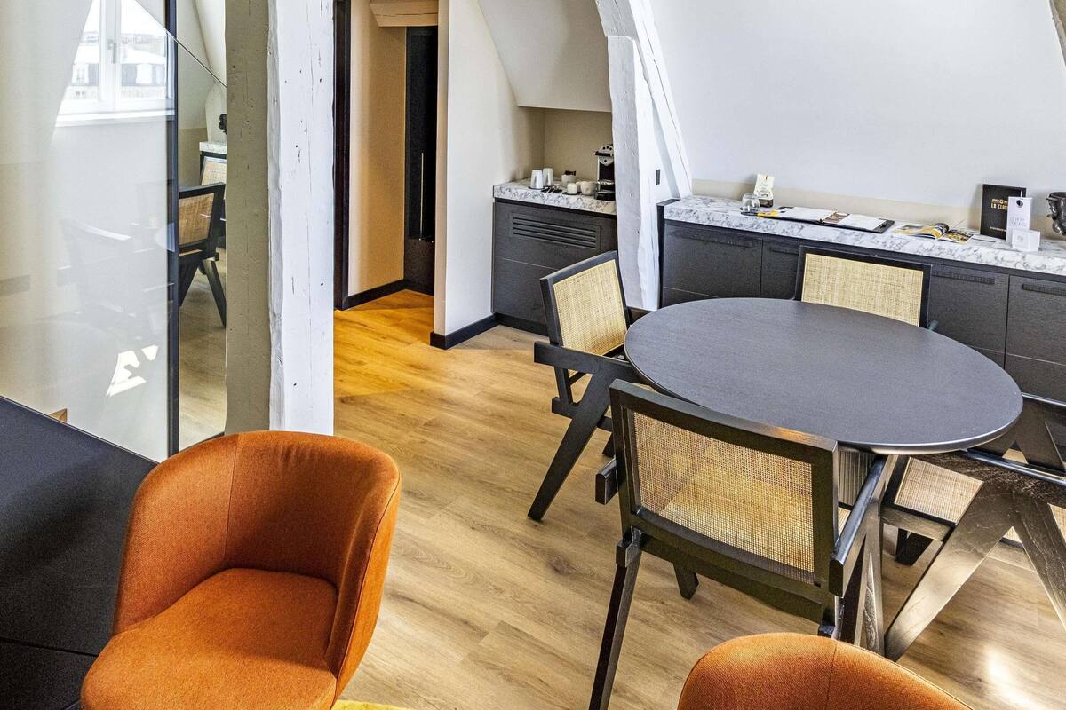 Ein modernes Loft-Zimmer mit Esstisch, zwei orangefarbenen Stühlen, einer Küchenzeile und Blick durch eine Glastür.