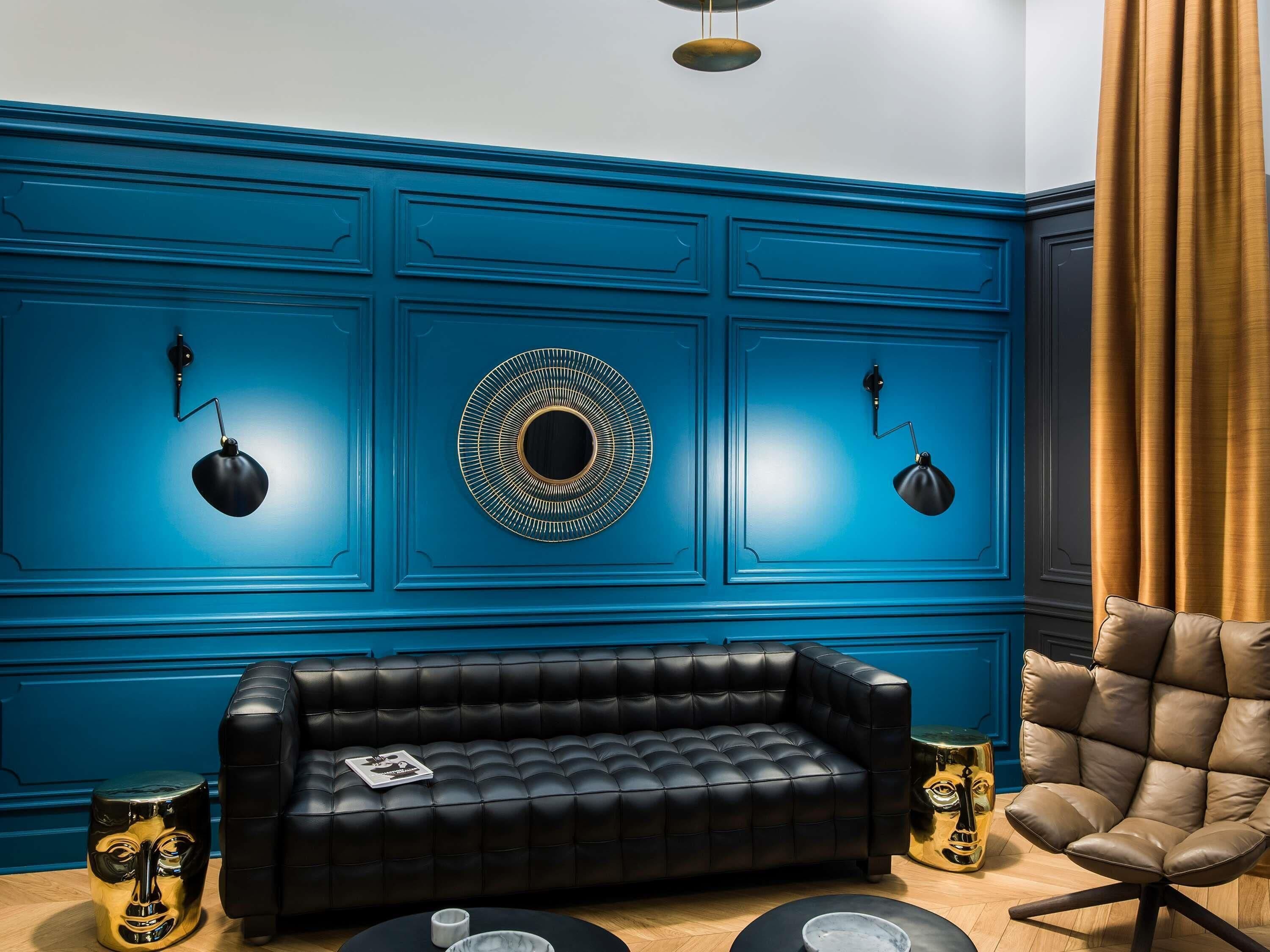 A room with a blue paneled wall, a black leather sofa, a brown leather armchair, and two black floor lamps.