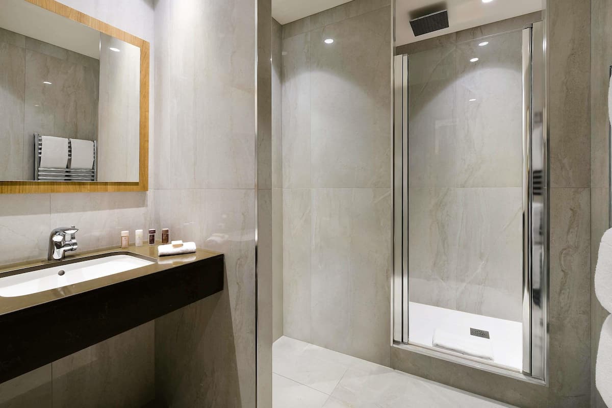 Une salle de bain moderne avec un grand miroir, un lavabo et une douche à l’italienne.