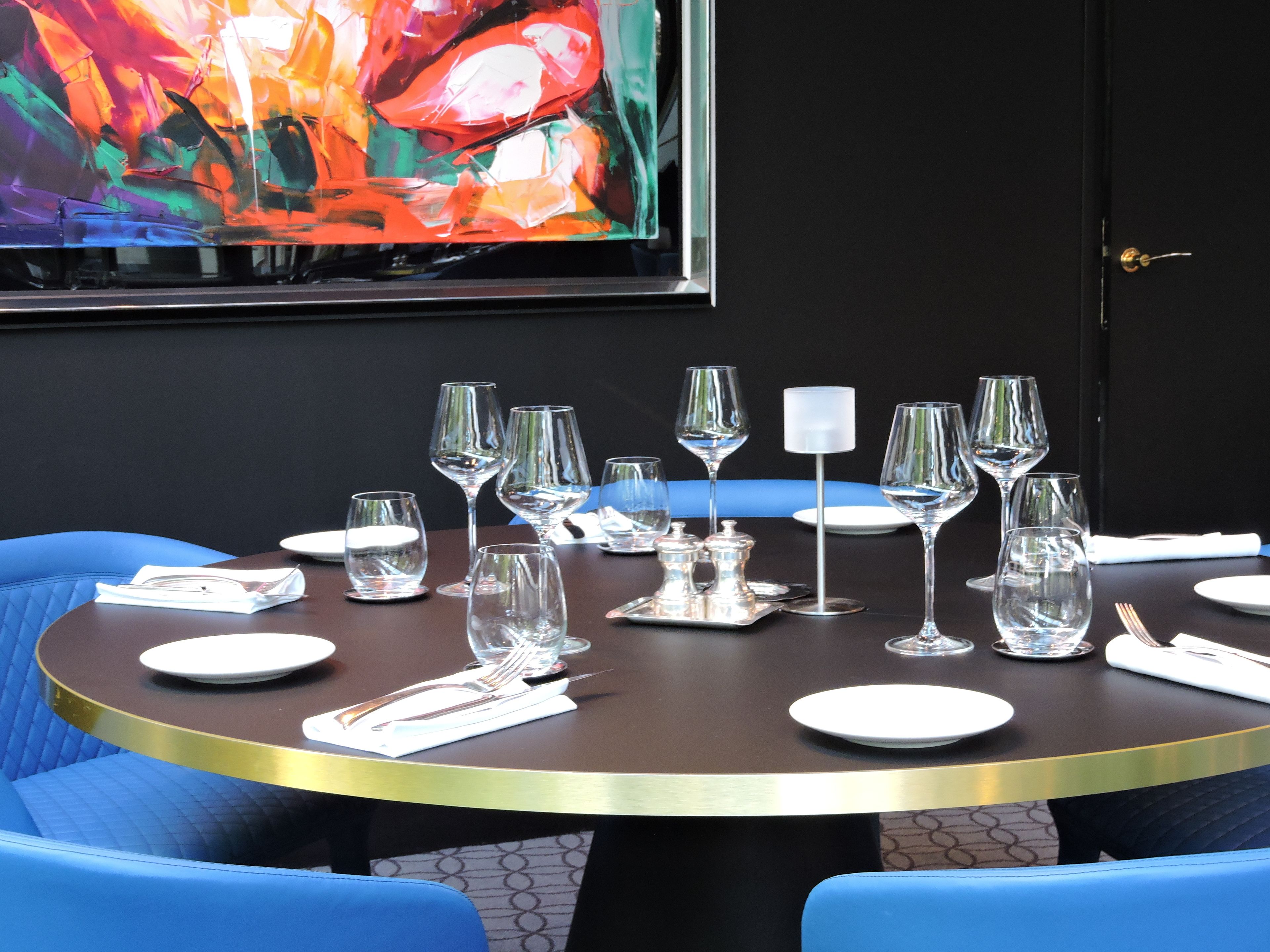 A dining table set with multiple wine glasses, plates, and cutlery, surrounded by blue upholstered chairs.