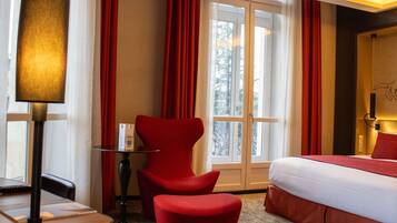 Una habitación de hotel con cama, escritorio con lámpara, silla y ventana con cortinas.