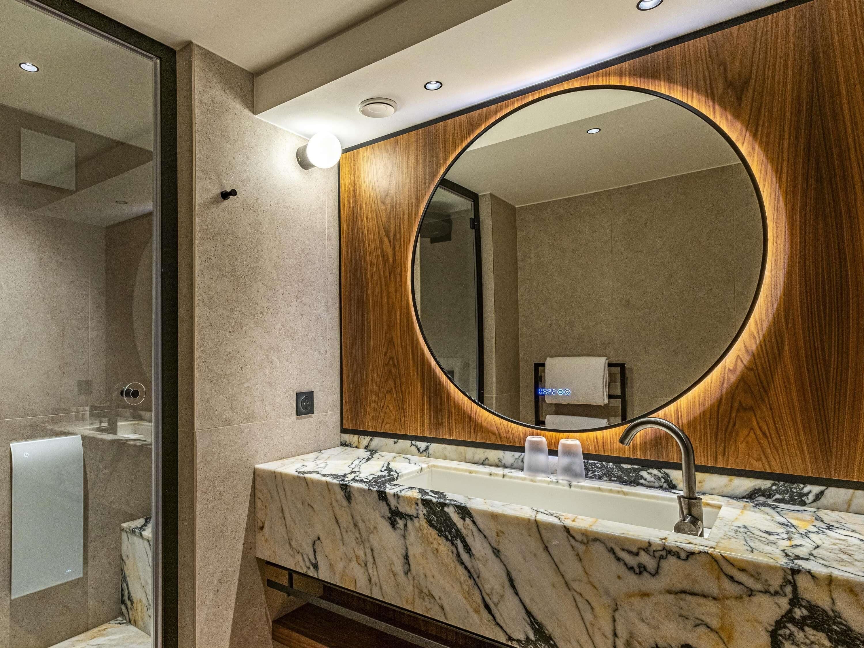 Un baño moderno con un lavabo de mármol, un espejo grande y un mueble de tocador de madera.