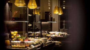 A buffet setup with various food items and beverages, illuminated by hanging lamps.