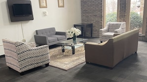 A spacious living area with a grey sofa, patterned armchair, and a coffee table with a vase of flowers. - Travelodge by Wyndham Vernon CT (Vernon)