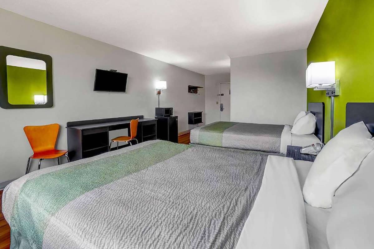 A hotel room with two beds, a desk, a chair, a TV, and a mirror.