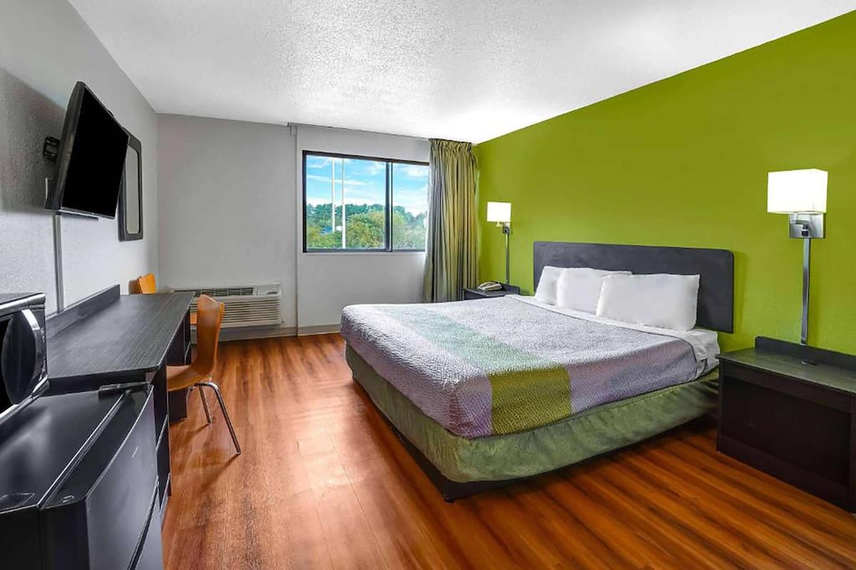 A hotel room with a bed, desk, chair, and a TV mounted on the wall.
