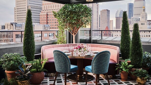 A rooftop dining area with a round table set for two, surrounded by plush seating and potted plants. - The Newbury Boston (Boston)