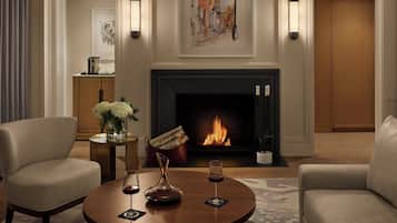 A cozy living room with a fireplace, two armchairs, a coffee table with wine glasses, and a painting above the fireplace.