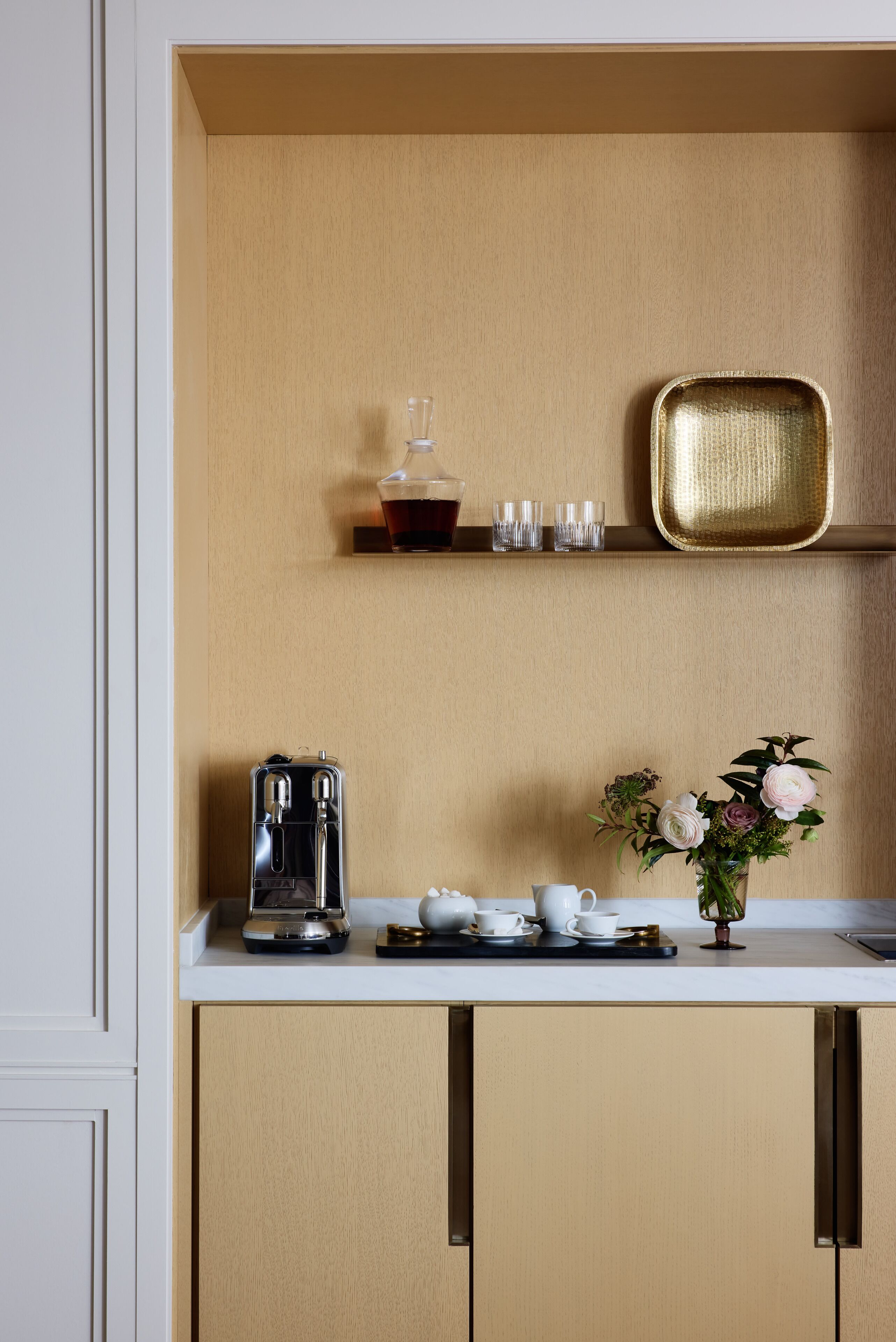 A compact kitchen with a coffee maker, cups, and a vase of flowers on the counter.