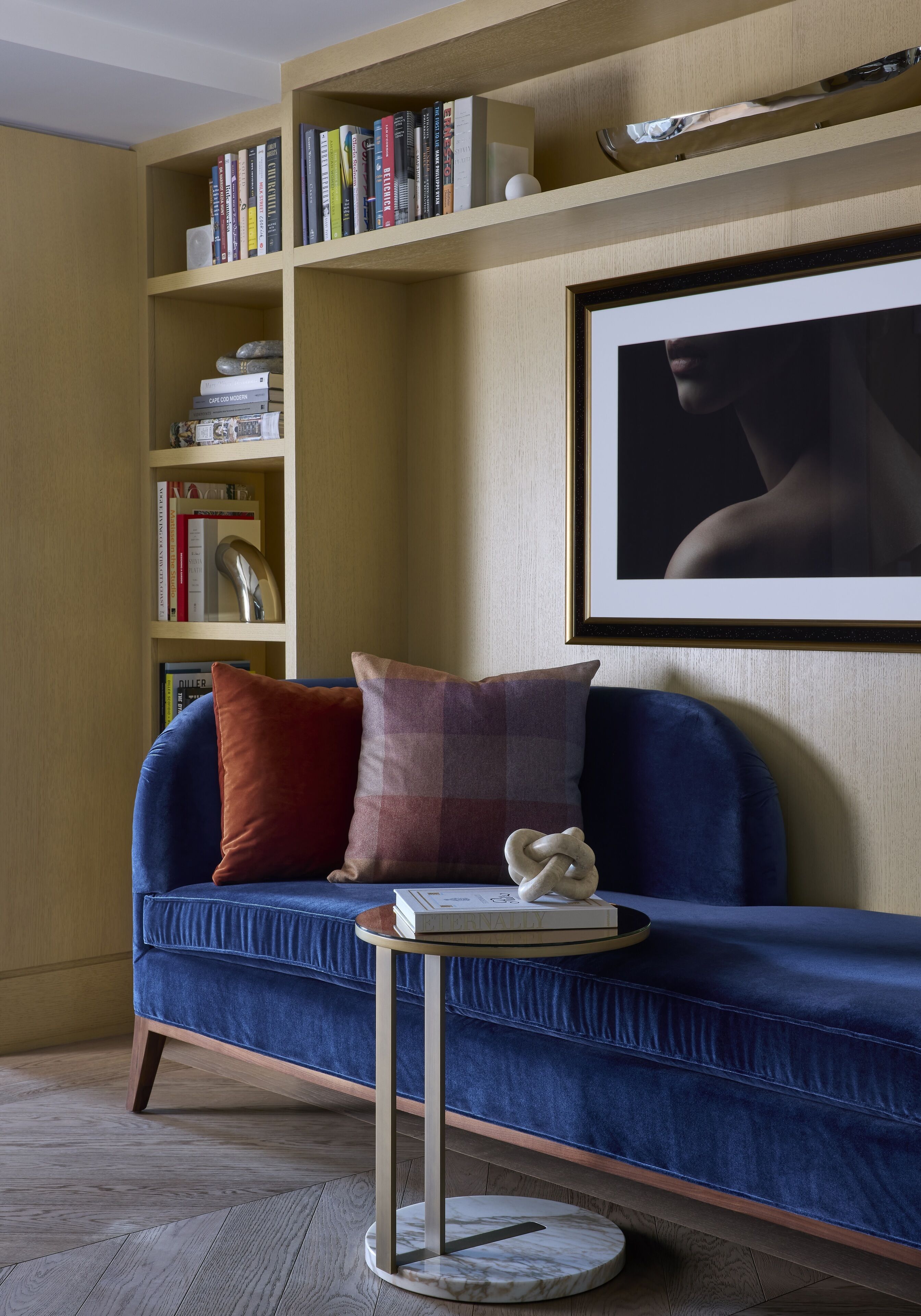 A cozy living room with a blue sofa, a small round table, and a bookshelf filled with books.