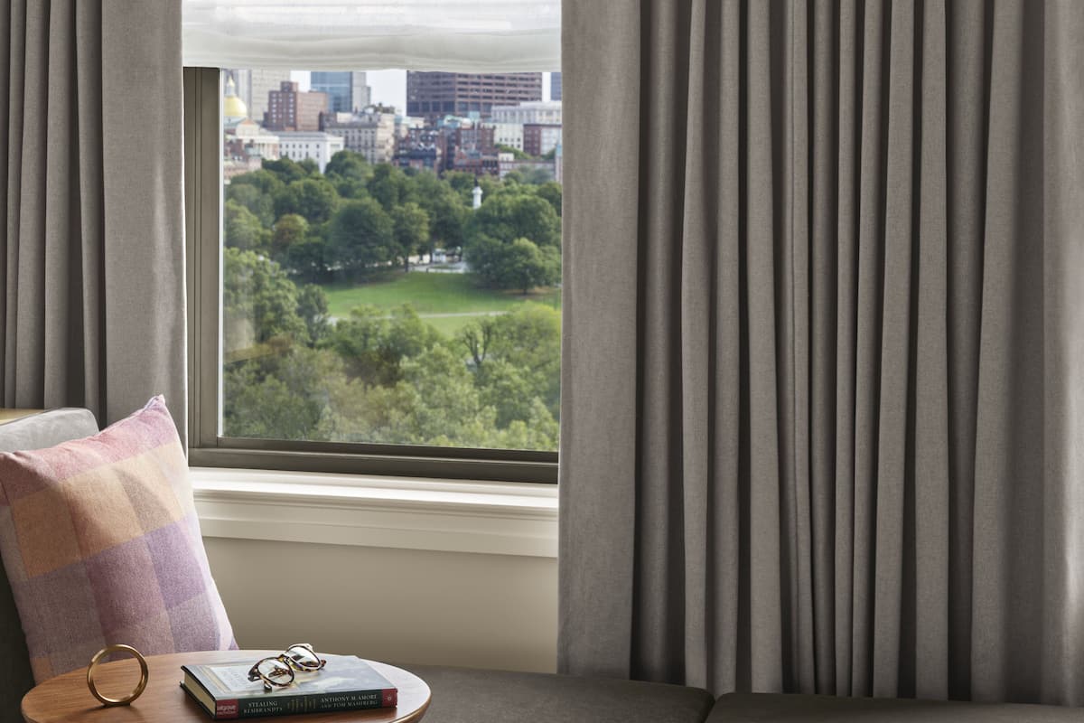 A room with a view of a cityscape and a park through a window with grey curtains.