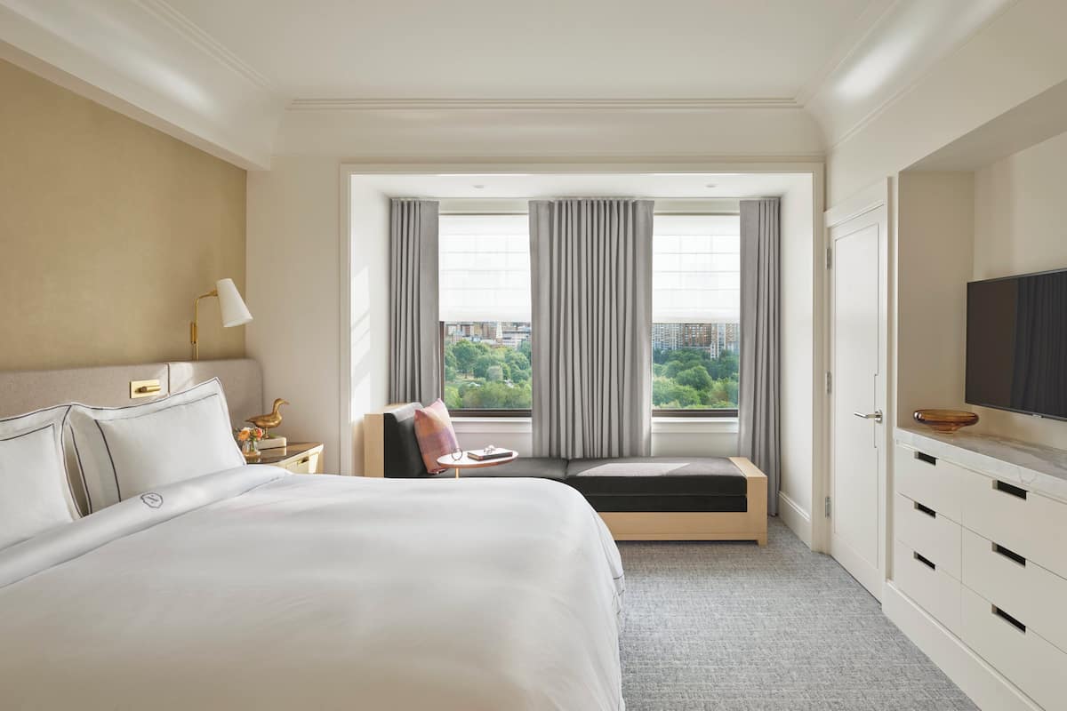 A hotel room with a large bed, a seating area with a view, a television, and a minibar.