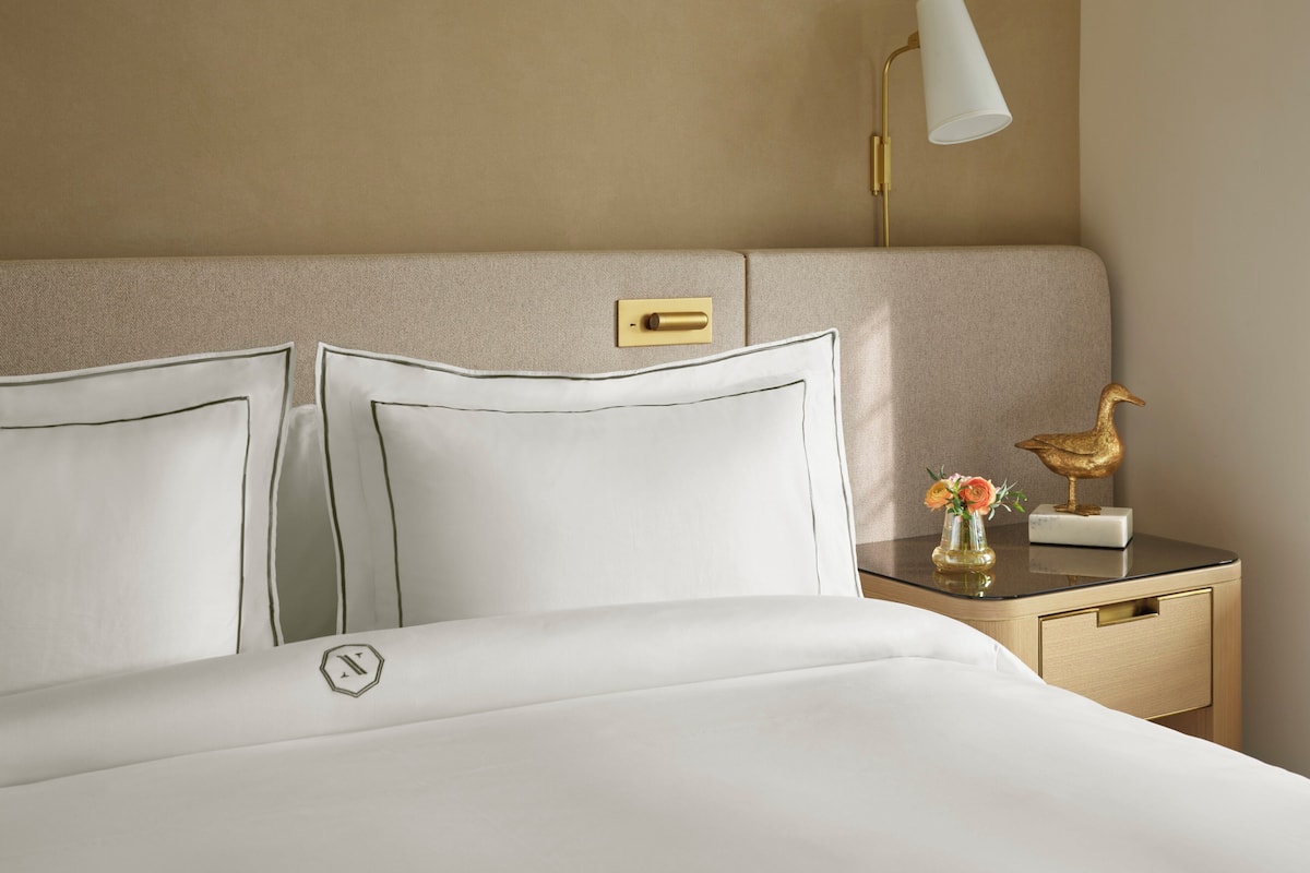 A neatly made bed with white linens and a gold-toned headboard.