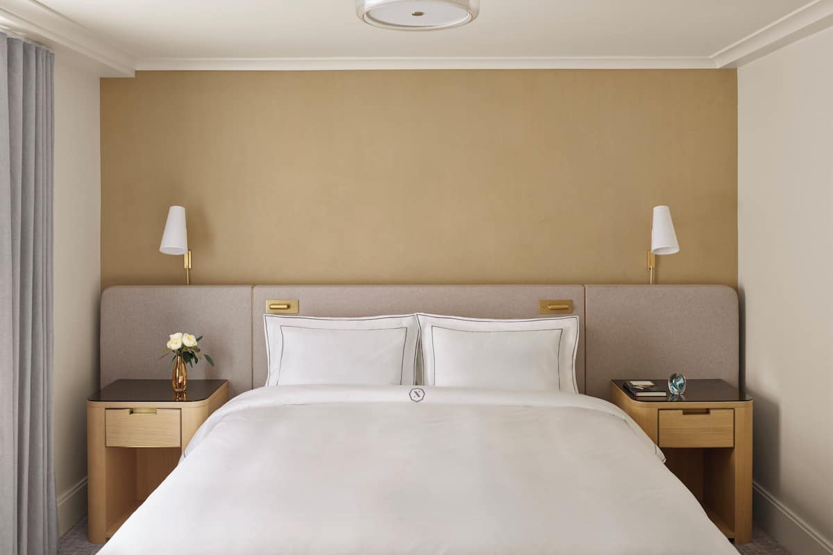 A hotel room with a large bed, two bedside tables with lamps, and a vase with flowers on one table.
