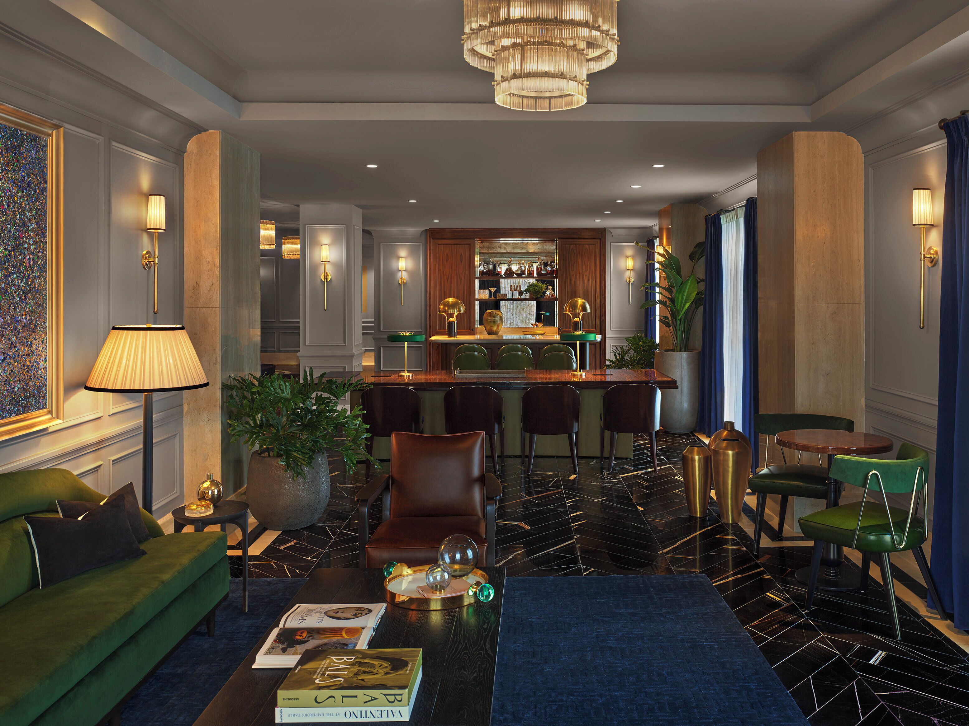 A modern hotel lobby with a bar area, green seating, and a chandelier.