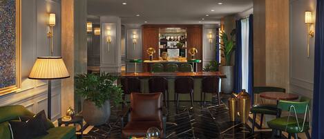 A modern hotel lobby with a bar area, green seating, and a chandelier.
