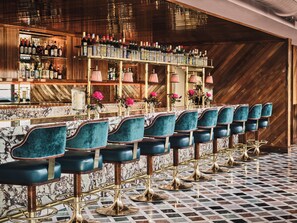 A bar area with a marble countertop, teal upholstered bar stools, and a wooden wall with a herringbone pattern.