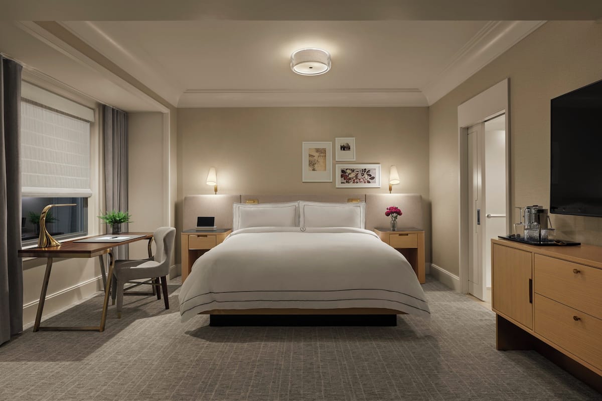 A modern hotel room with a large bed, a desk, and a TV.