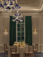 A formal dining room with a chandelier, green curtains, and a table set for four.