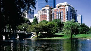 A river with a bridge, a park with trees, and a mix of historic and modern buildings in the background.