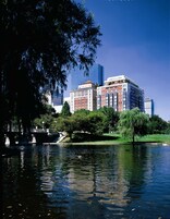 A river with a bridge, a park with trees, and a mix of historic and modern buildings in the background.
